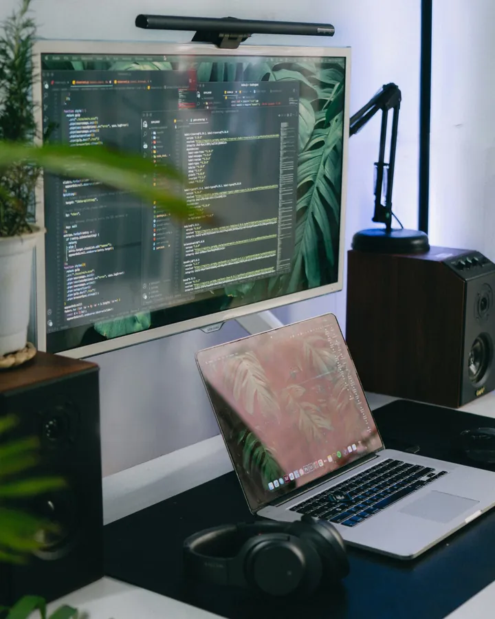 Poste de travail : un grand écran avec du code au-dessus d’un ordinateur portable, entouré de plantes.
